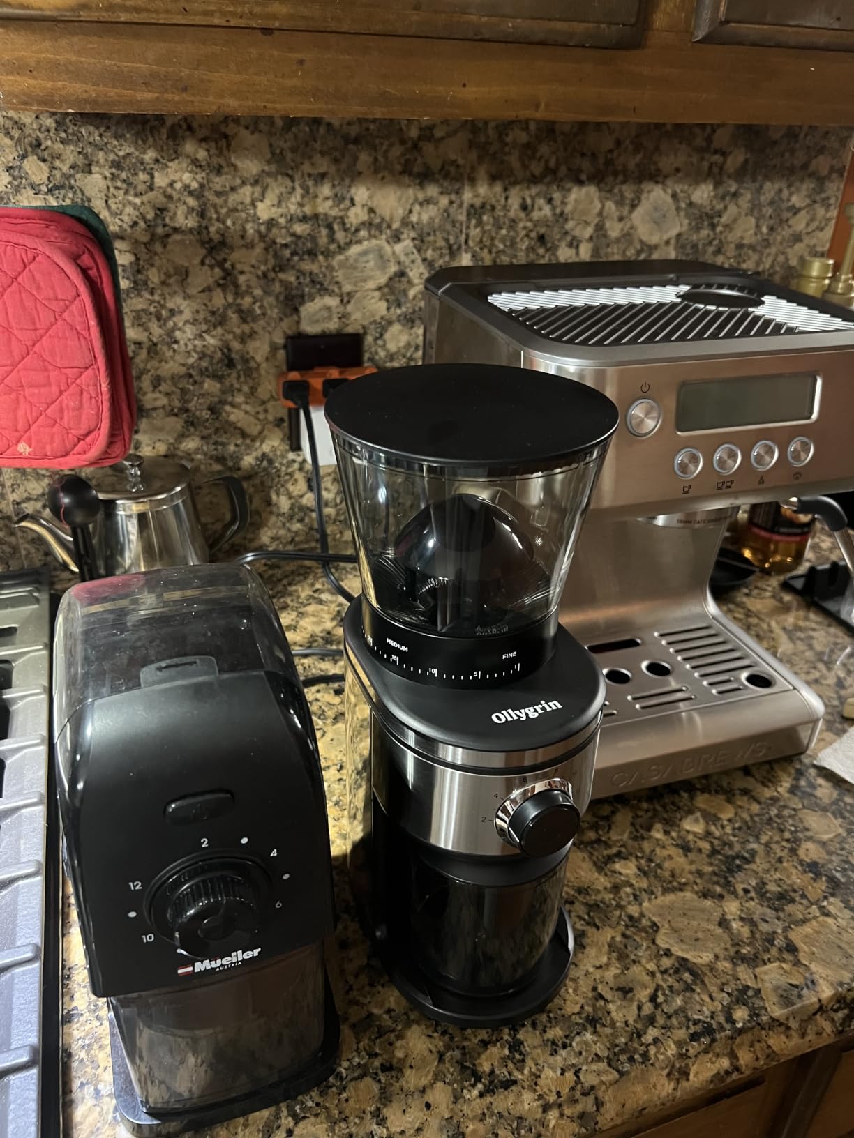 Ollygrin conical burr grinder on a granite counter next to a home espresso machine