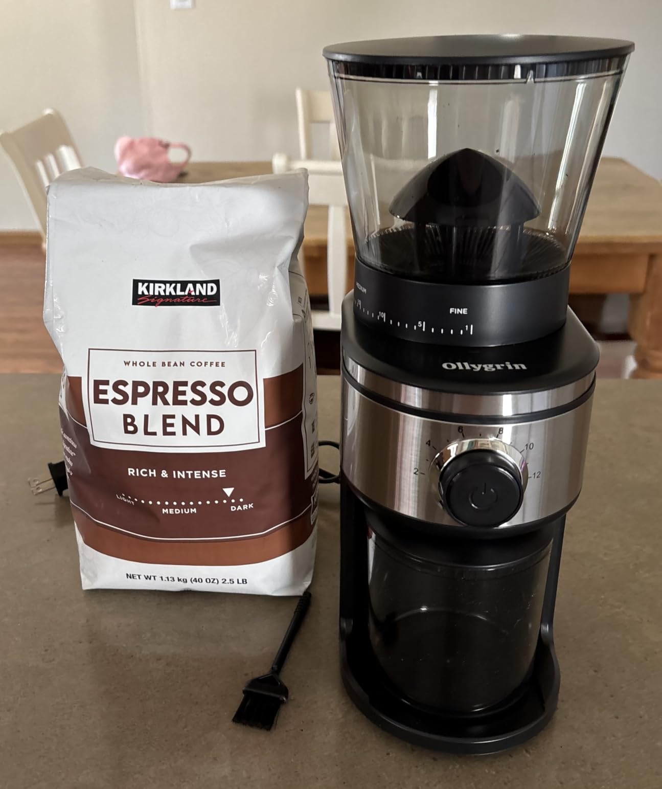 Ollygrin 30-setting conical burr grinder next to a bag of whole bean espresso blend and the included cleaning brush
