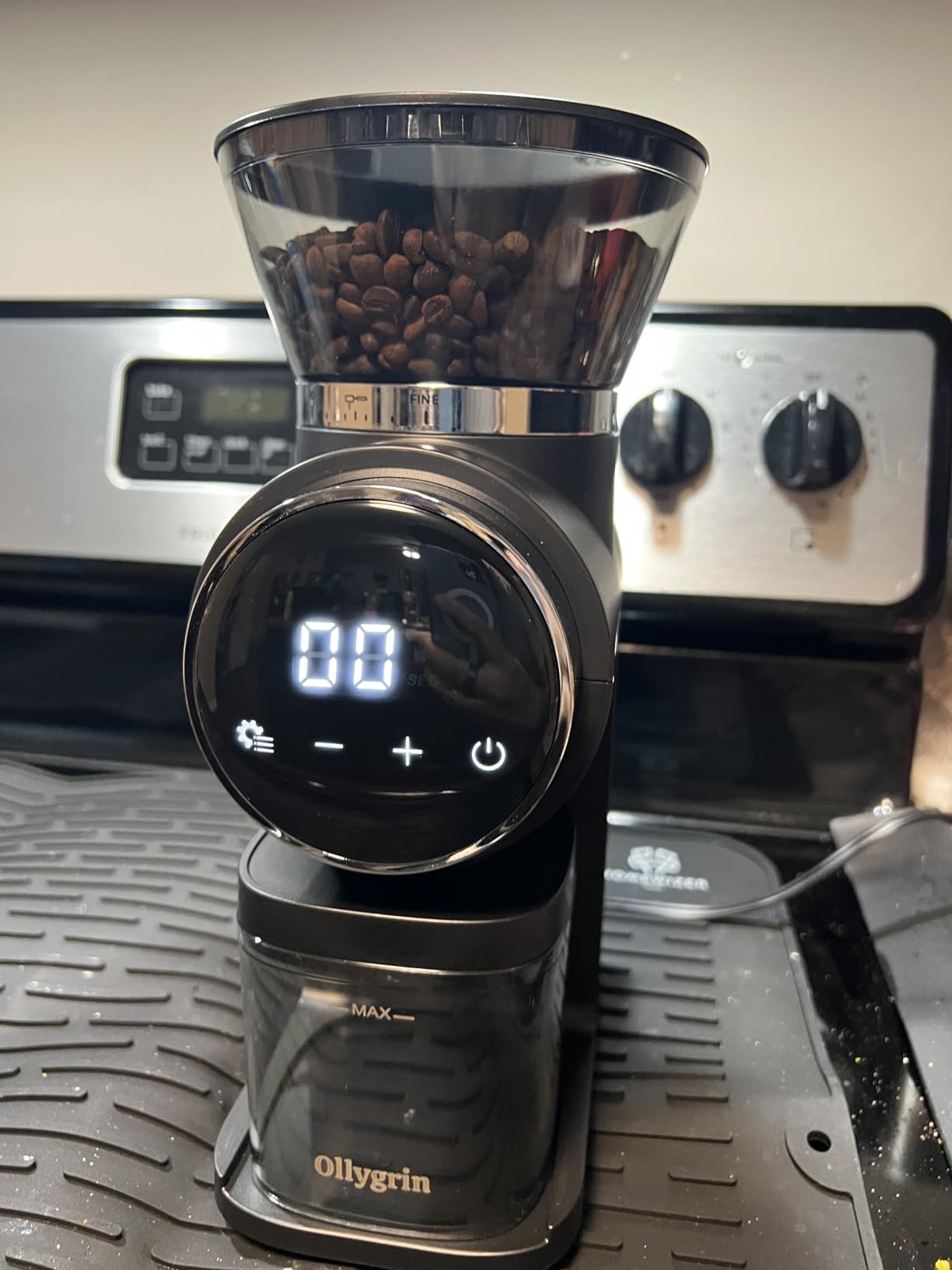 Ollygrin grinder with a digital display and a full bean hopper in front of a kitchen stove