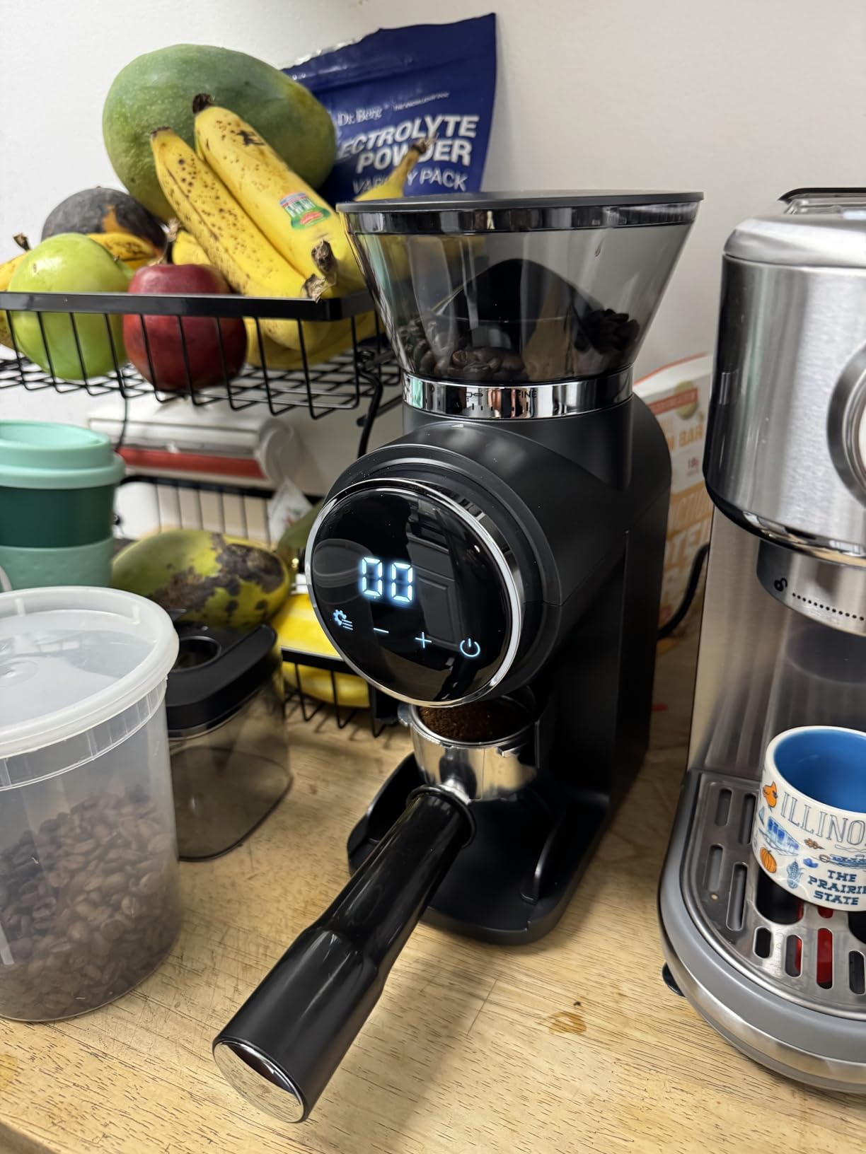 Ollygrin grinder with a digital display beside an espresso machine, with a portafilter resting in front of it