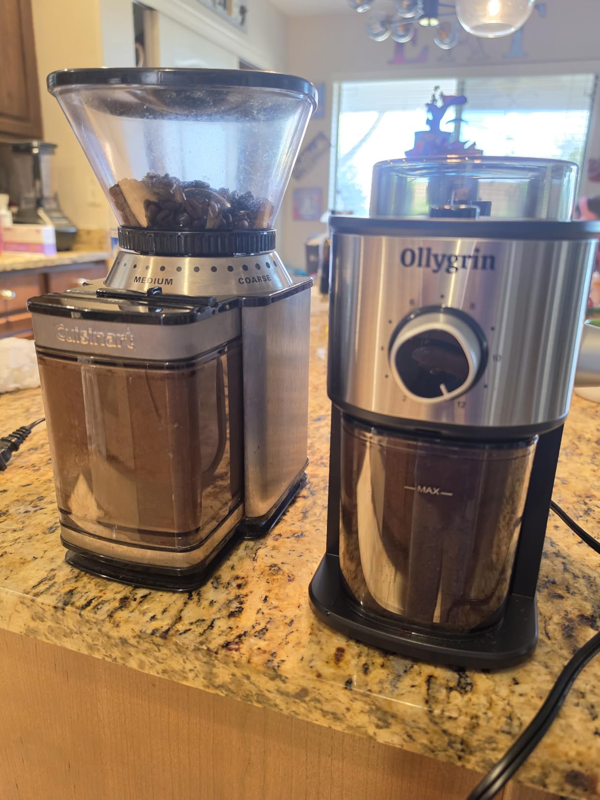 Stainless Ollygrin flat burr grinder standing next to an older coffee grinder on a granite counter