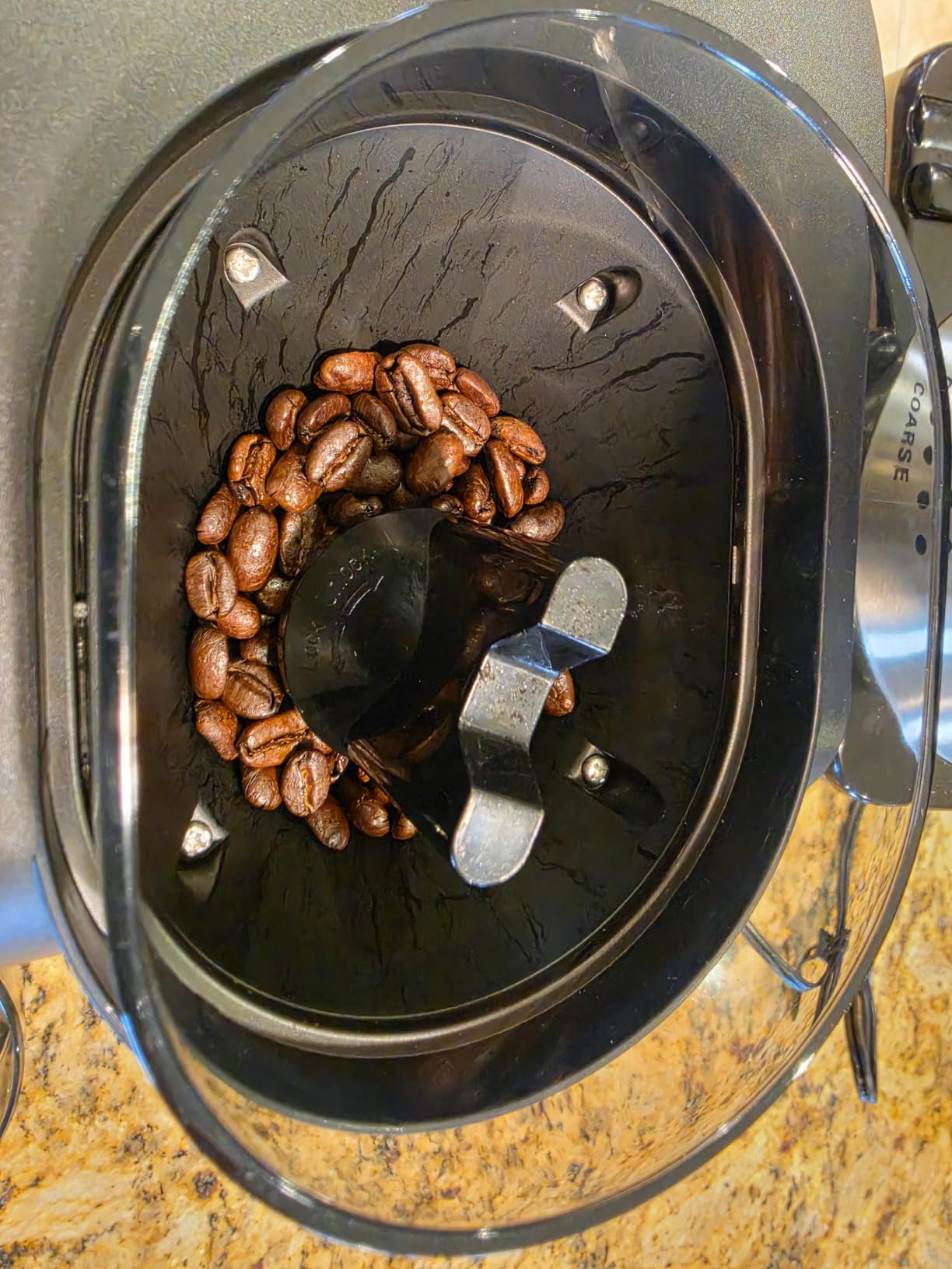 Top-down view into an Ollygrin hopper with roasted coffee beans around the burr opening